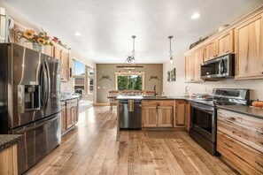 A spacious kitchen with wooden cabinets, stainless steel appliances, and a central island. - Klassy Lodge - New Lodge • Private Hot Tub & Game Room (Sturgis)