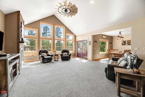 A spacious living room with a high ceiling, large windows, and a fireplace. - Klassy Lodge - Private Hot Tub & Game Room (Sturgis)
