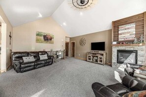 A spacious living room with a leather sofa, a flat-screen TV, a fireplace, and a wall-mounted clock. - Klassy Lodge - New Lodge • Private Hot Tub & Game Room (Sturgis)