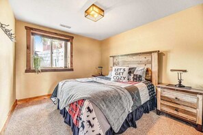 Ein Schlafzimmer mit Bett, Nachttisch, Kommode, Fenster und Deckenleuchte.