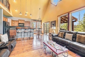 A spacious living area with a leather sofa, a dining table with chairs, and a kitchen in the background.