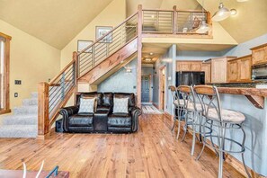 A spacious living area with a wooden staircase, a leather sofa, and a kitchen with wooden cabinets and bar stools.