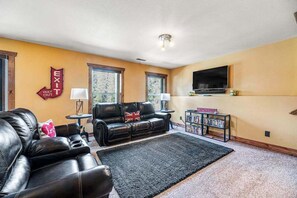 Ein Wohnzimmer mit einer schwarzen Ledersofa, einem Bücherregal und einem an der Wand befestigten Flachbildfernseher.