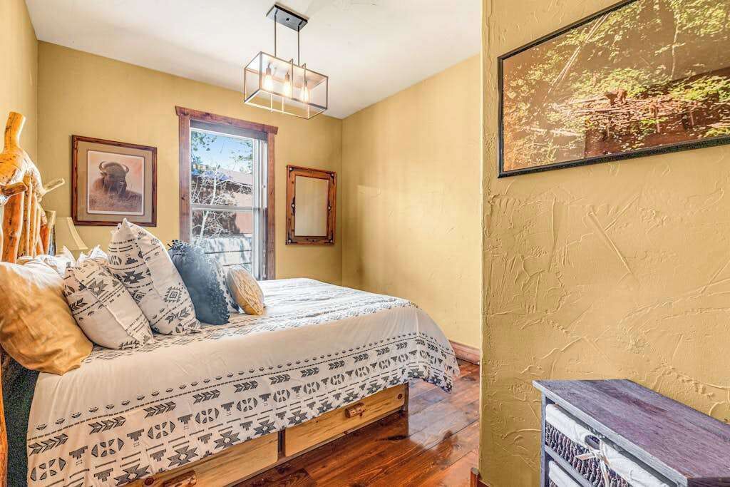 Ein Schlafzimmer mit einem Bett, einem hölzernen Kopfteil, einer Pendelleuchte und einem gerahmten Bild an der Wand.