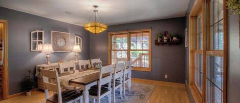 A dining room with a wooden table and chairs, a chandelier, and large windows.
