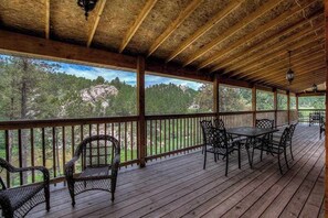 A covered outdoor deck with wooden flooring, metal chairs, and a table. - Eagle Pine Lodge - Dog-Friendly Home w/ Pool Access (Custer)