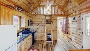 A compact kitchen with wooden walls, a central staircase, and a small window. - Meandering Moose Cabin - Secluded Wood Cabin w/ Big Deck (Florissant)