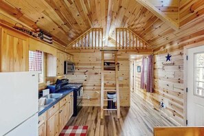 A compact kitchen with wooden walls, a central staircase, and a small window. - Meandering Moose Cabin - Secluded Wood Cabin w/ Big Deck (Florissant)