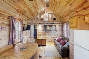 A cabin interior with a dining table, sofa, and a mounted television. - Secluded Pine Cabin • Big Deck • Trails Nearby (Florissant)