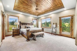 A bedroom with a large bed, wooden headboard, a wooden bench, a ladder, and a view of a balcony. - Cedar Lodge on 17- Hot Tub Home Near Mt Rushmore (Sturgis)