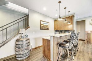 A kitchen with a bar area, wooden cabinets, and a bar stool seating arrangement. - Cedar Lodge on 17- Hot Tub Home Near Mt Rushmore (Sturgis)