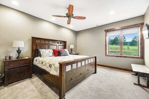 A bedroom with a wooden bed, bedside tables, a ceiling fan, and a window with a view of a field. - Cedar Lodge on 17- Hot Tub Home Near Mt Rushmore (Sturgis)