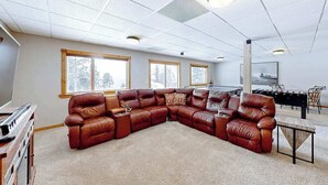 A spacious living room with a large L-shaped leather sofa, a wooden coffee table, and a foosball table.