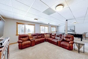 A spacious living room with a large L-shaped leather sofa, a wooden coffee table, and a foosball table.