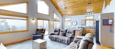 A spacious living area with a high ceiling, large windows, and a modern kitchen.