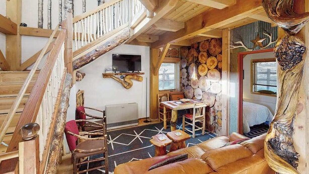 A rustic interior with a wooden staircase, a fireplace, a dining area, and a sofa. - Treehouse Retreat • Pikes Peak Views with Hot Tub (Florissant)