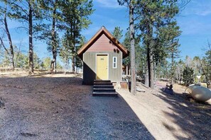 A small wooden cabin with a yellow door, surrounded by trees, and a gravel path leading to it.