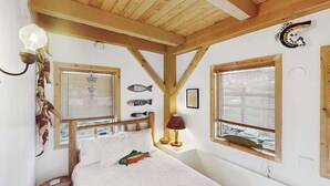 A bedroom with a wooden ceiling, a bed with white bedding, two windows with blinds, and wall-mounted fish decorations. - Treehouse Retreat • Pikes Peak Views with Hot Tub (Florissant)