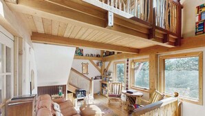 A spacious living area with a high ceiling, wooden beams, a large window, and a cozy seating arrangement. - Treehouse Retreat • Pikes Peak Views with Hot Tub (Florissant)