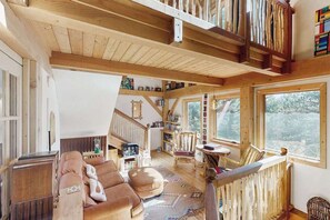 Ein geräumiger Wohnbereich mit hoher Decke, Holzbalken, einem großen Fenster und einer gemütlichen Sitzecke.
