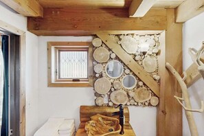 Ein Badezimmer mit einem Holzbachttopf, einem Fenster mit Gitterstäben und einer Wand, die mit Holzscheiben und Spiegeln verziert ist.