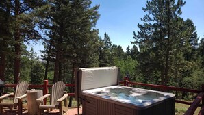 A hot tub with a wooden deck, surrounded by a red railing, set in a forested area. - Treehouse Retreat • Pikes Peak Views with Hot Tub (Florissant)