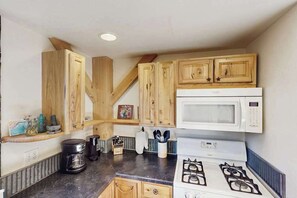 A compact kitchen with wooden cabinets, a microwave, a stove, and a coffee maker.