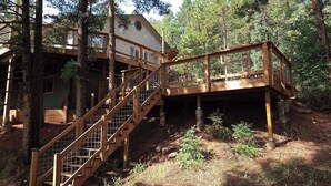 Eine Holztreppe führt zu einer Terrasse mit Geländer, umgeben von Bäumen.