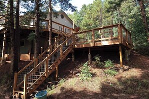 Eine Holztreppe führt zu einer Terrasse mit Geländer, umgeben von Bäumen.