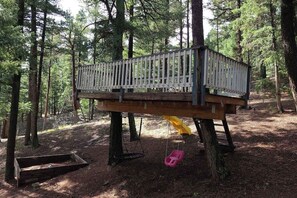 En träkonstruerad terrass i ett skogsområde, med en gunga och en bänk.