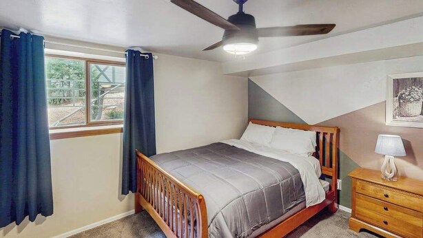 Ein Schlafzimmer mit einem Einzelbett, einem Nachttisch, einem Deckenventilator und einem Fenster mit Vorhängen.