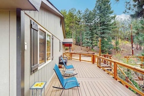 A wooden deck with outdoor seating and a view of a forested area. - The Lookout at Woodland Park - Dog-Friendly Mtn Home • Fenced Yard (Woodland Park)
