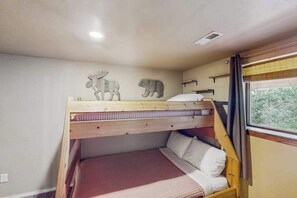 Un lit superposé avec une tête de lit ornée de sculptures d’animaux, une fenêtre offrant une vue agréable et une étagère fixée au mur.