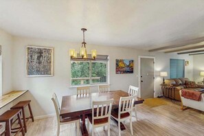 Un coin repas avec une table en bois et des chaises blanches, un lustre et des œuvres d’art accrochées aux murs.