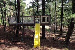 En träkonstruerad terrass i ett skogsområde, med en stege som leder upp till den.