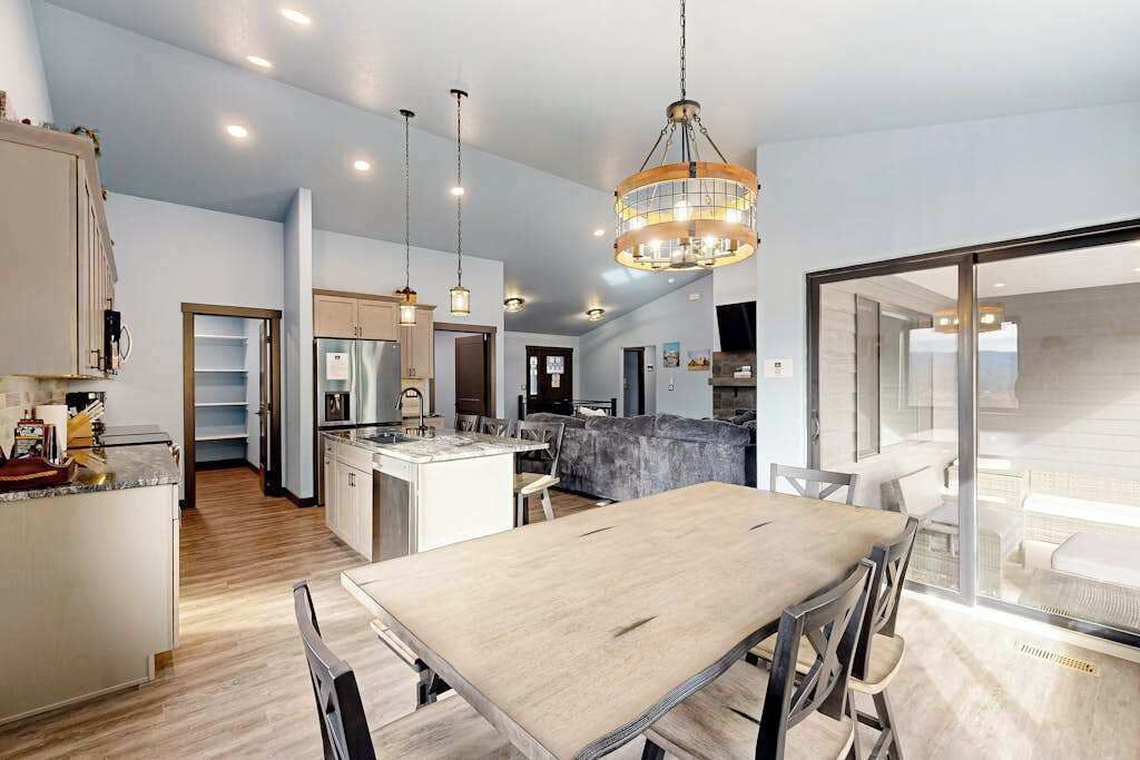A spacious kitchen with a dining area, a chandelier, and a view through a glass door.