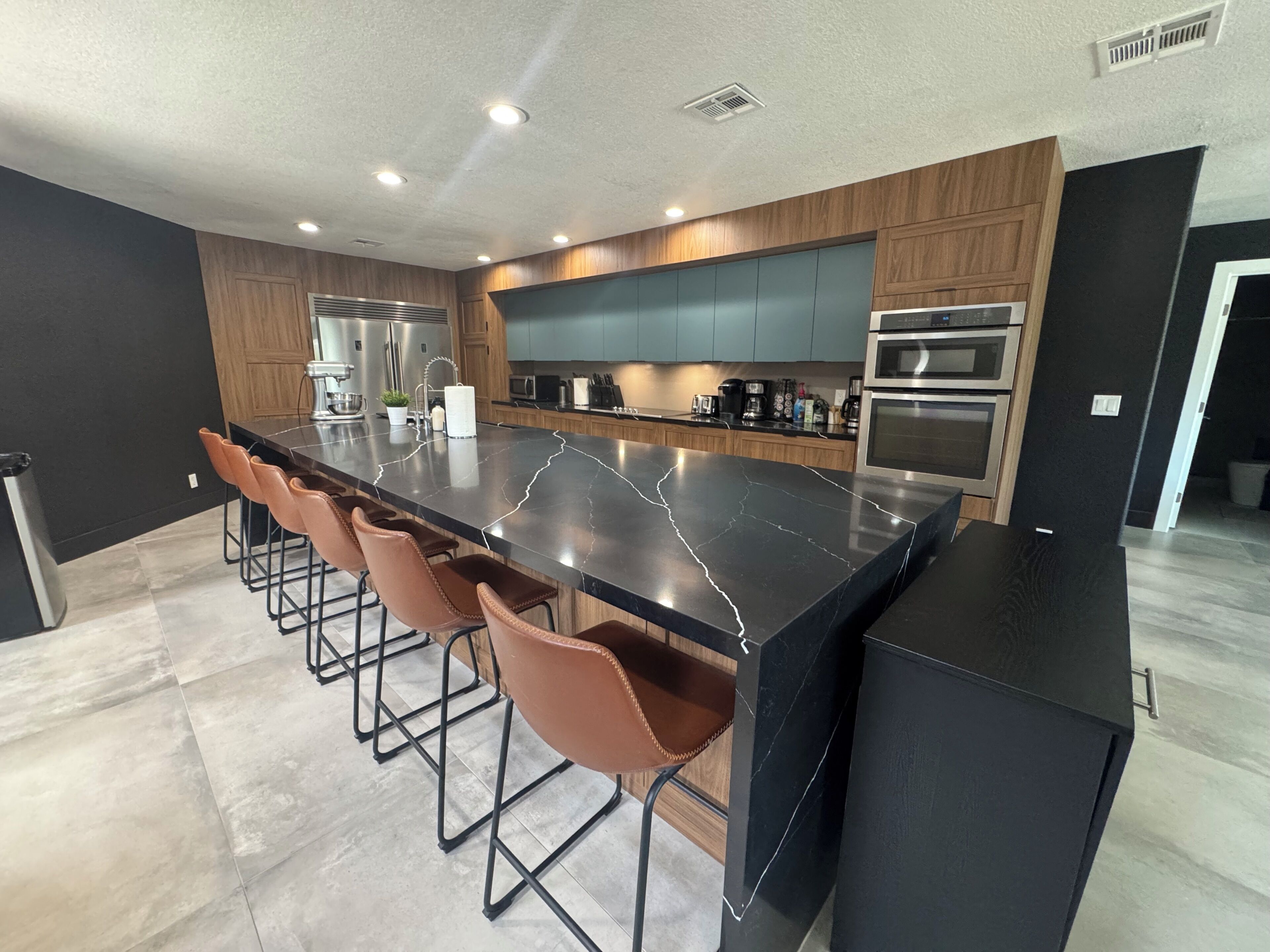 A modern kitchen with a large island, bar stools, stainless steel appliances, and wooden cabinetry.