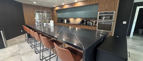 A modern kitchen with a large island, bar stools, stainless steel appliances, and wooden cabinetry.