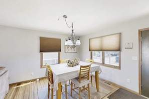 A dining area with a table, chairs, a chandelier, and a window with blinds. - Stratobowl Escape - Dual-Unit Home Near Black Hills Fun (Rapid City)