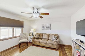 A living room with a ceiling fan, a sofa, a chair, a television, and a window. - Stratobowl Escape - Dual-Unit Home Near Black Hills Fun (Rapid City)