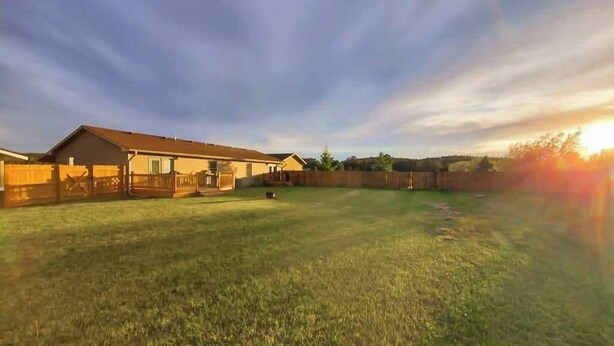A residential property with a large grassy yard, a wooden fence, and a house with a sloped roof. - Stratobowl Escape - Dual-Unit Home Near Black Hills Fun (Rapid City)