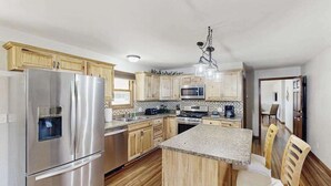 A modern kitchen with stainless steel appliances, wooden cabinets, and a central island with seating. - Stratobowl Escape - Dual-Unit Home Near Black Hills Fun (Rapid City)