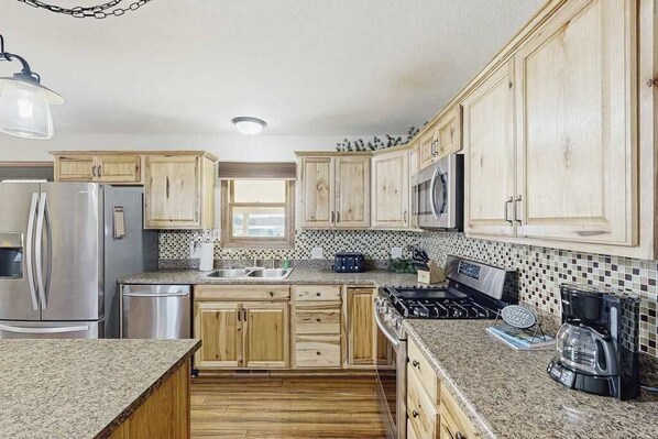 A kitchen with wooden cabinets, stainless steel appliances, a granite countertop, and a coffee maker. - Stratobowl Escape - Dual-Unit Home Near Black Hills Fun (Rapid City)