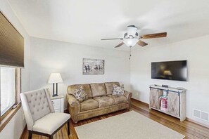 A living room with a sofa, a chair, a television, a ceiling fan, and a painting on the wall. - Stratobowl Escape - Dual-Unit Home Near Black Hills Fun (Rapid City)
