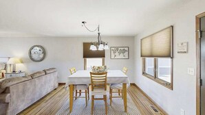 A dining area with a table, chairs, a chandelier, a sofa, a lamp, and a window with blinds. - Stratobowl Escape - Dual-Unit Home Near Black Hills Fun (Rapid City)