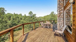 Eine Holzterrasse mit einer Steinmauer, Gartenmöbeln und Blick auf einen Wald.
