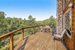 A wooden deck with a stone wall, outdoor furniture, and a view of a forest. - Aces and Eights Lodge (Sturgis)