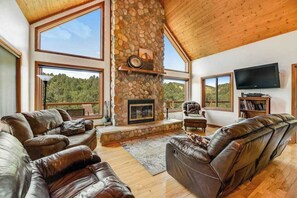 A spacious living room with leather sofas, a stone fireplace, large windows, and a flat-screen TV. - Aces and Eights Lodge (Sturgis)