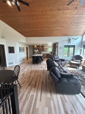 A spacious living area with a wooden floor, a large leather sofa, a dining table with chairs, and a kitchen in the background. - Aces and Eights Lodge (Sturgis)