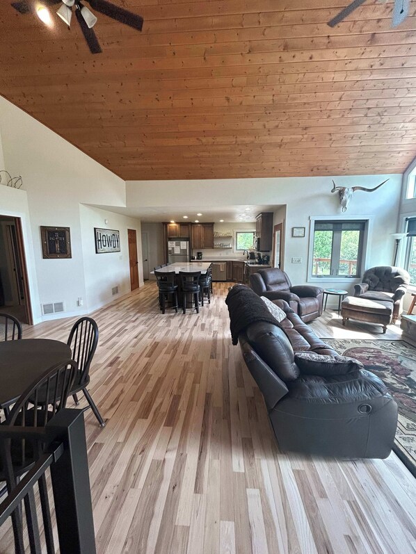 A spacious living area with a wooden floor, a large leather sofa, a dining table with chairs, and a kitchen in the background. - Aces and Eights Lodge (Sturgis)